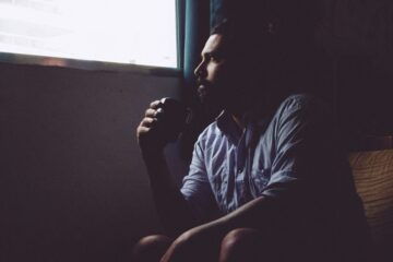 Man sitting in a dark room with a cup of tea. Image: Unsplash.